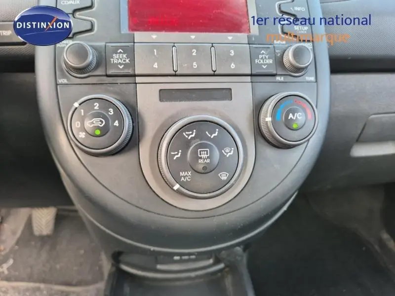 Vue rapprochée du tableau de bord central de la KIA SOUL 1.6 16v Plug 2010, montrant les commandes de climatisation et radio.