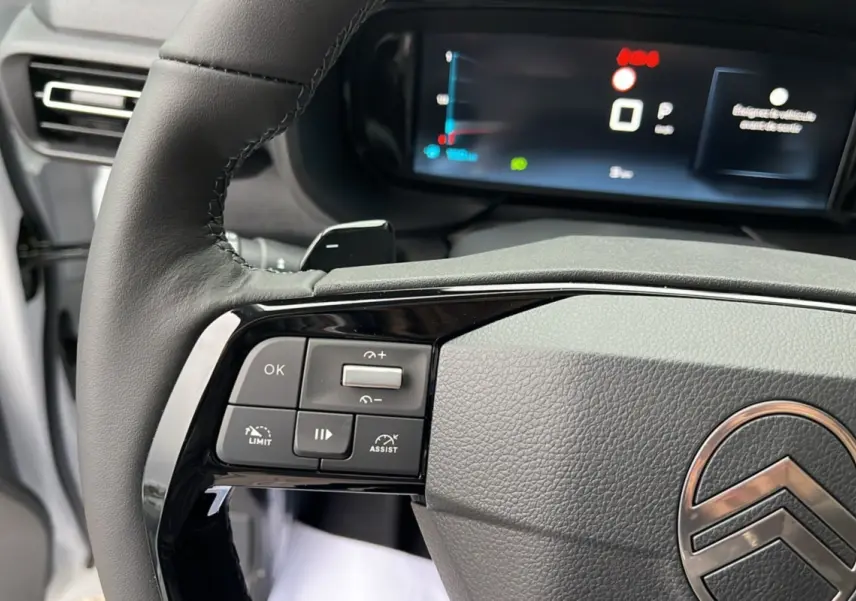 Gros plan sur le volant cuir multifonctions du Citroën Berlingo Kaolin white, avec commandes intégrées et tableau de bord numérique en arrière-plan.