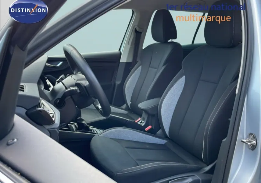 Vue intérieure côté conducteur du Skoda Kamiq gris argent métal 2025, montrant les sièges en tissu noir et gris et le volant multifonction.