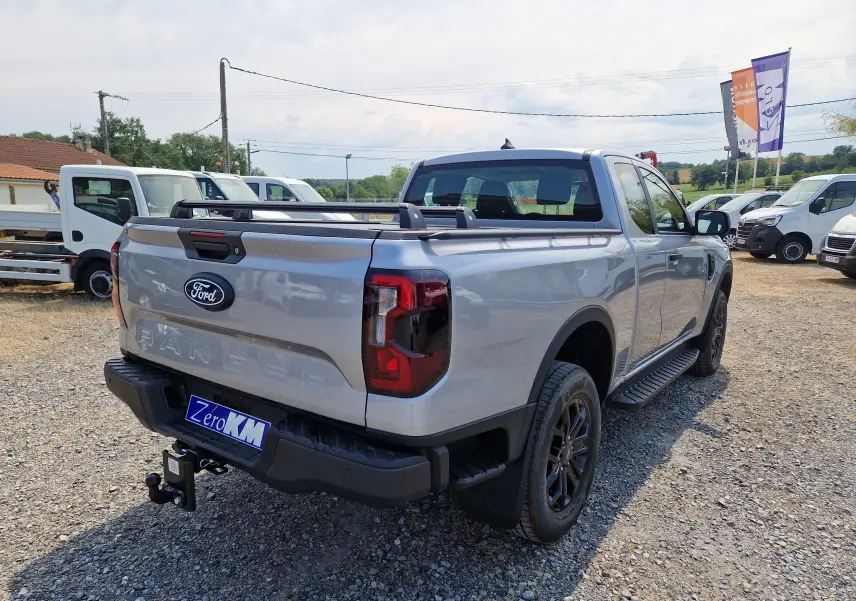 Vue 3/4 arrière droite du Ford Ranger Super Cabine gris Iconic avec ridelle coulissante et barres de plateau visibles.