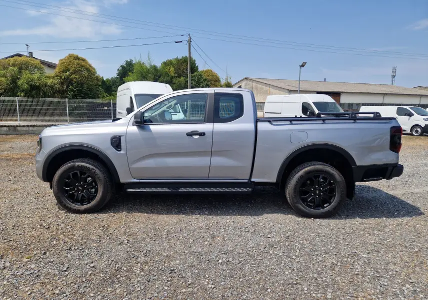 Vue de profil côté gauche d'un Ford Ranger Super Cabine gris Iconic avec barres de plateau et jantes noires.