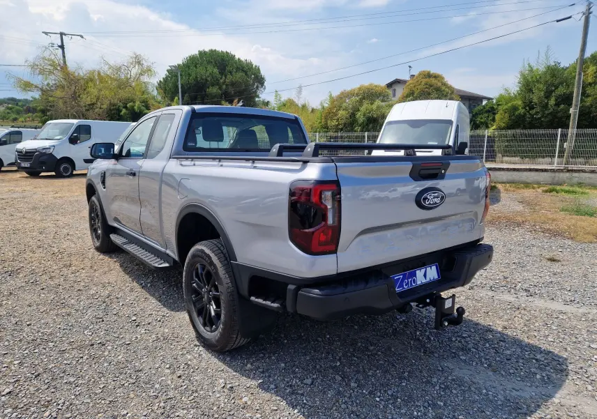 Ford Ranger Super Cabine gris Iconic vu en 3/4 arrière droit, avec ridelle renforcée et barre de plateau noire.