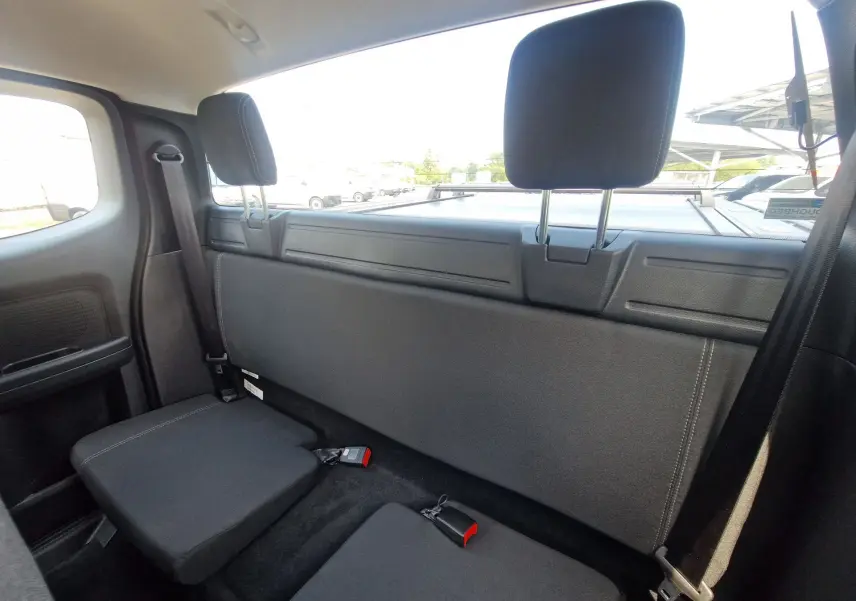 Vue intérieure arrière du Ford Ranger Super Cabine 2026, sièges arrière rabattus en tissu noir avec ceintures visibles.
