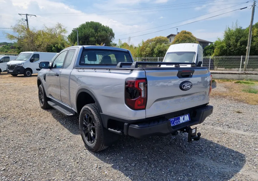 Vue 3/4 arrière droite du Ford Ranger Super Cabine gris Iconic avec barres de plateau et attelage visible.