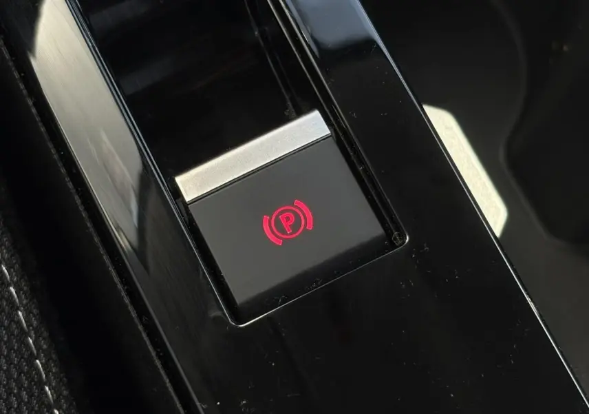 Gros plan sur le bouton de frein de stationnement électrique rouge, console centrale noire de la Citroën C4 Hybrid 2025.