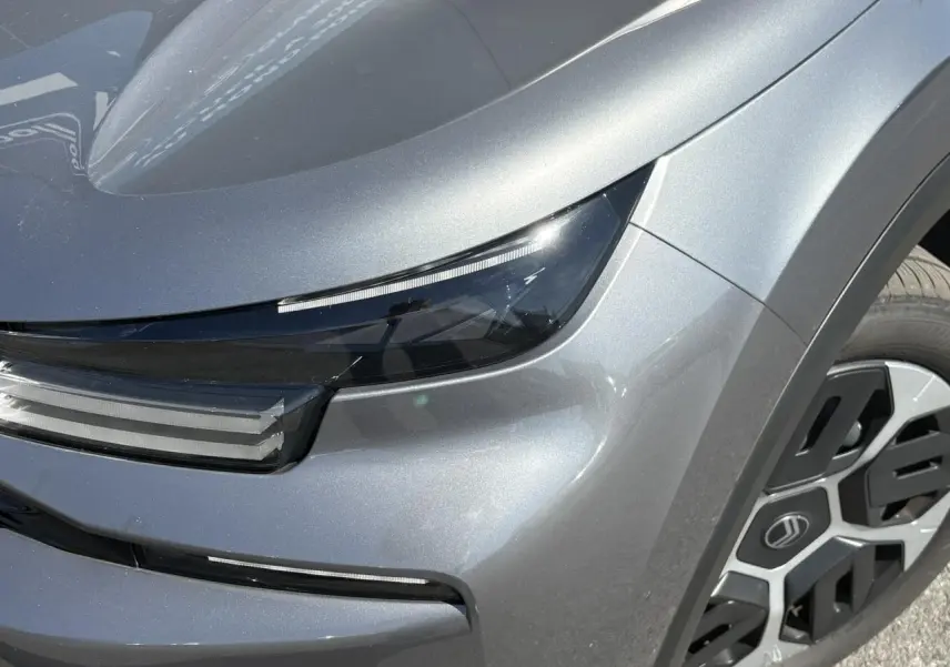 Gros plan sur le phare avant droit et la roue d’une Citroën C4 Hybrid 145 gris Mercury avec détails lumineux modernes.