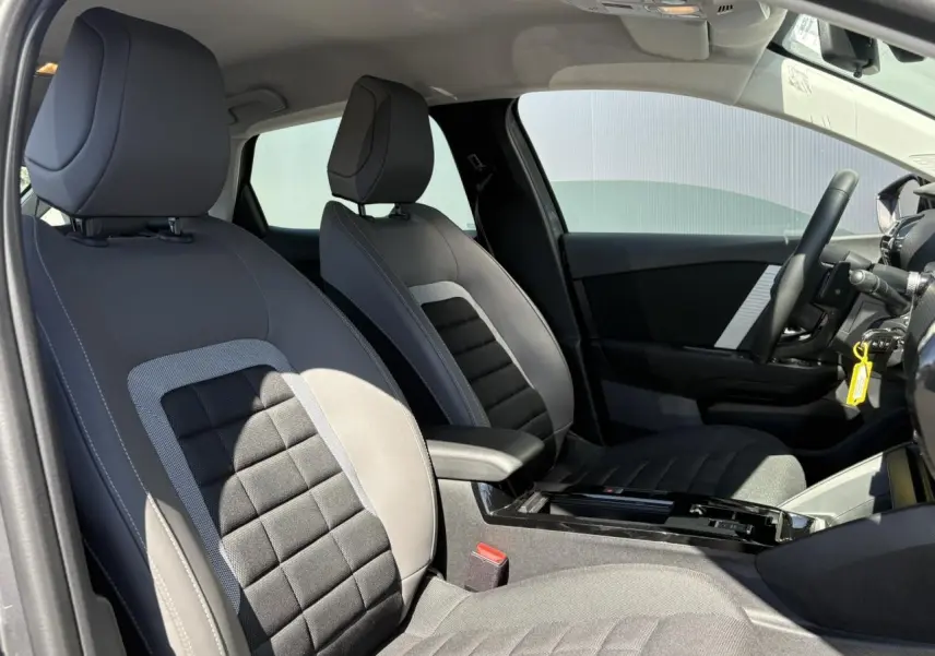 Intérieur avant de la Citroën C4 Hybrid 2025, vue côté droit, sièges tissu noir et gris avec accoudoir central.