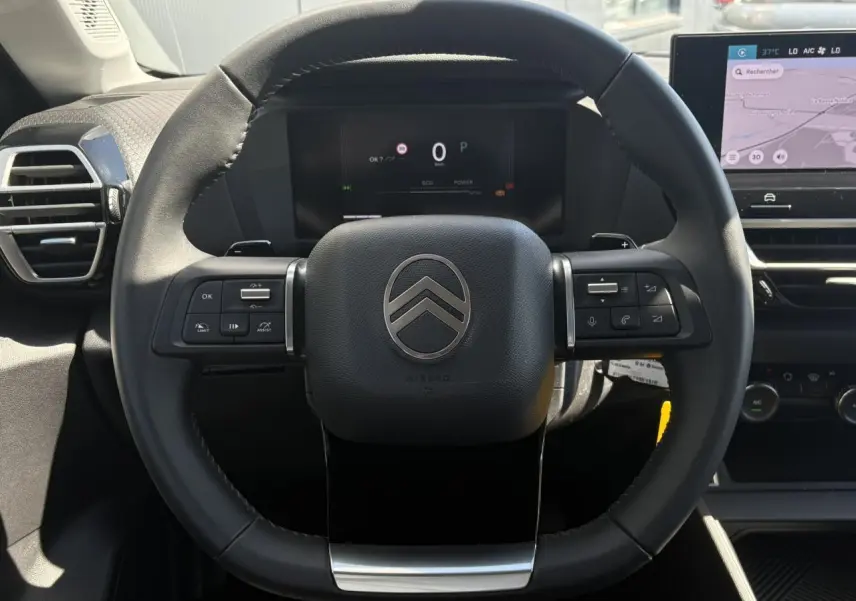 Vue rapprochée du volant cuir noir de la Citroën C4 Hybrid 2025 avec tableau de bord numérique et écran tactile.