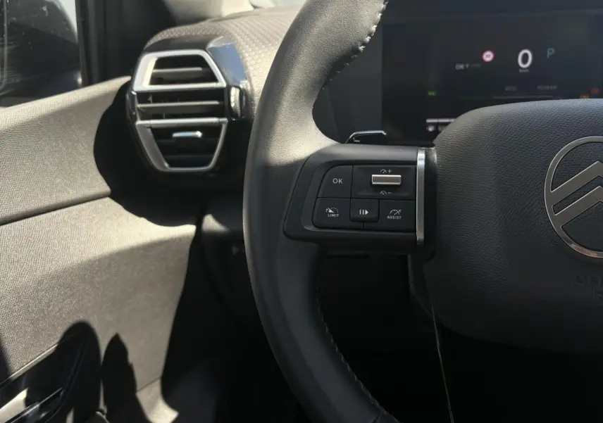 Gros plan sur le volant noir et les commandes à gauche du tableau de bord d'une Citroën C4 Hybrid 2025.
