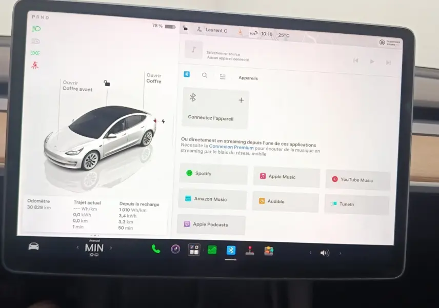 Écran tactile central de Tesla Model 3 blanc 2022 montrant interface multimédia et vue 3/4 avant du véhicule.