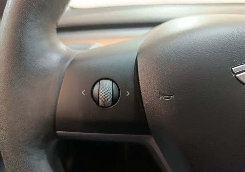 Gros plan sur le volant noir de la Tesla Model 3 2022 avec molette de commande et logo partiel visible.