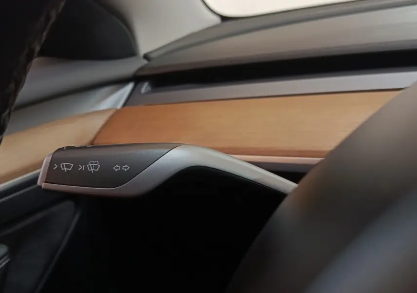 Détail intérieur du levier de clignotant et essuie-glace dans une Tesla Model 3 2022 avec tableau de bord en bois clair.