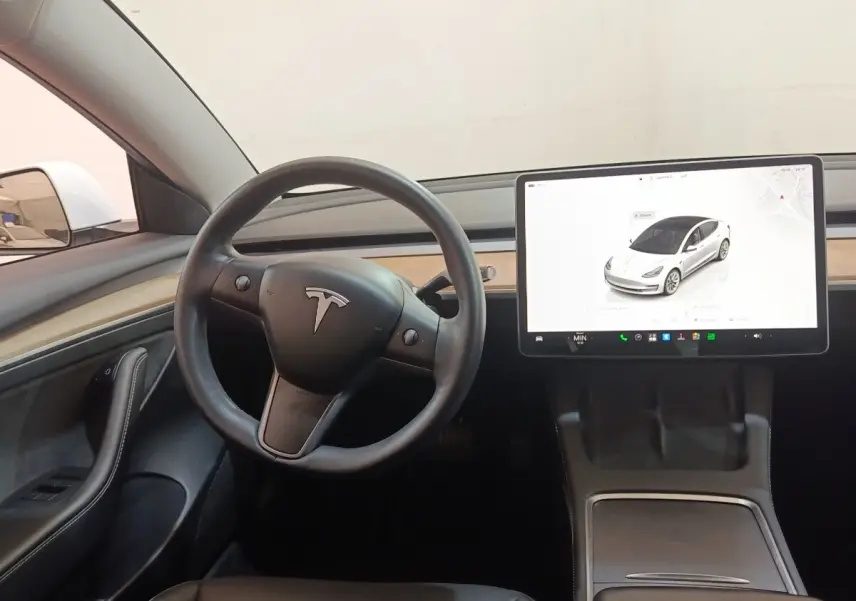 Intérieur Tesla Model 3 blanc 2022, vue du poste de conduite avec volant multifonctions et grand écran tactile central.
