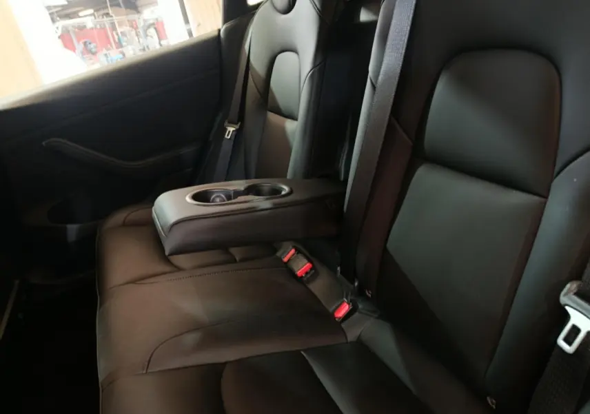 Vue intérieure montrant la banquette arrière noire avec accoudoir central et porte-gobelets dans une Tesla Model 3 Grande Autonomie.