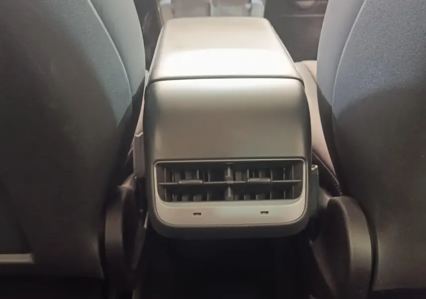 Vue rapprochée de la console centrale arrière noire entre les sièges avant d'une Tesla Model 3 blanche.