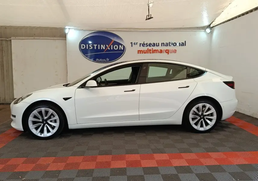 Profil latéral gauche d'une Tesla Model 3 blanche 2022, avec jantes distinctives et poignées affleurantes.