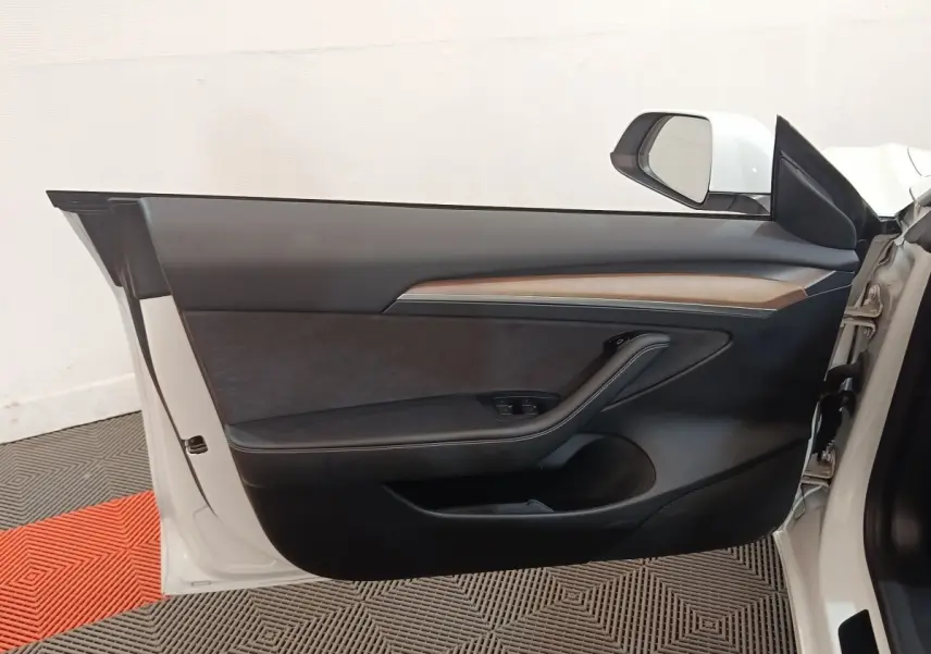 Porte avant gauche ouverte d'une Tesla Model 3 blanche, intérieur noir avec insert bois et commandes électriques.