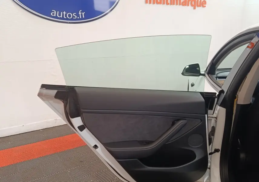 Porte arrière droite ouverte d'une Tesla Model 3 blanche, intérieur noir avec panneau de porte épuré.