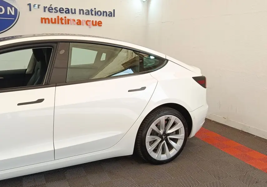 Profil arrière droit d'une Tesla Model 3 blanche 2022, avec jantes distinctives et vitres teintées.