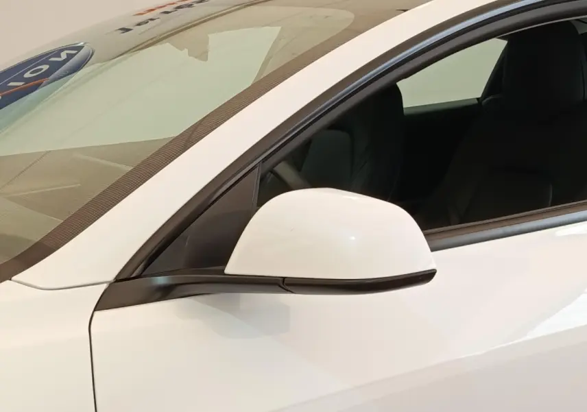 Gros plan sur le rétroviseur côté gauche d'une Tesla Model 3 blanche avec intérieur noir visible par la fenêtre ouverte.