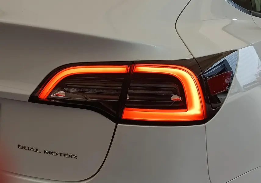 Gros plan sur le feu arrière droit allumé d'une Tesla Model 3 blanche avec logo Dual Motor visible.