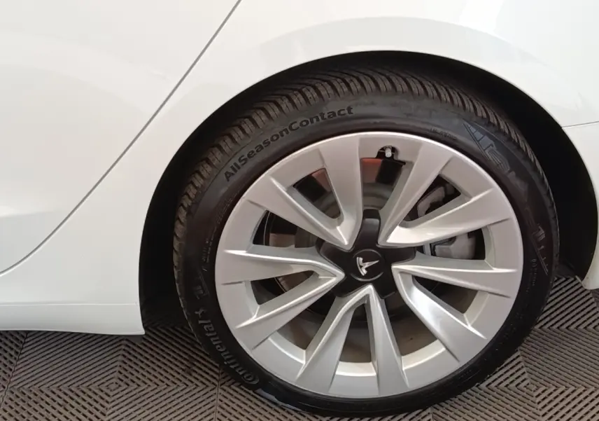 Gros plan sur la roue arrière droite blanche d'une Tesla Model 3 Grande Autonomie avec jante argentée distinctive.