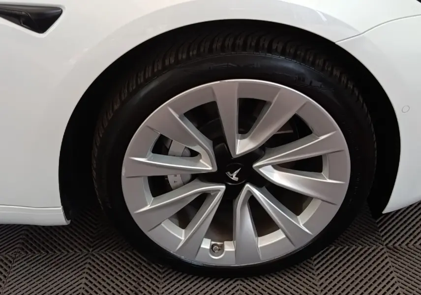 Gros plan sur la roue avant gauche argentée d'une Tesla Model 3 blanche, mettant en valeur la jante au design aérodynamique.