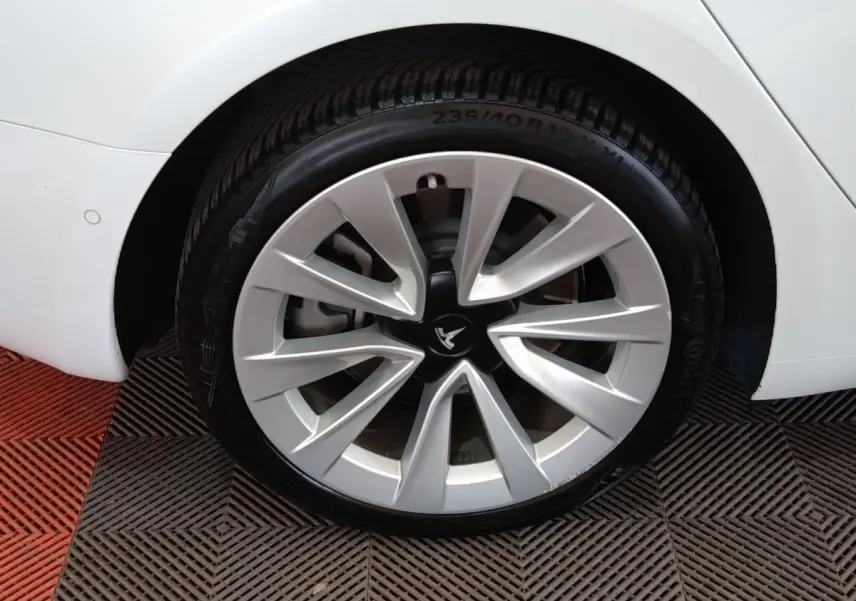 Gros plan sur la roue arrière droite d'une Tesla Model 3 blanche, mettant en valeur la jante aérodynamique distinctive.