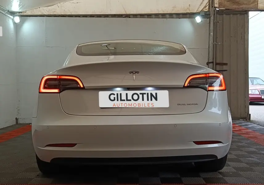 Vue arrière d'une Tesla Model 3 Grande Autonomie blanche avec feux LED allumés dans un garage.