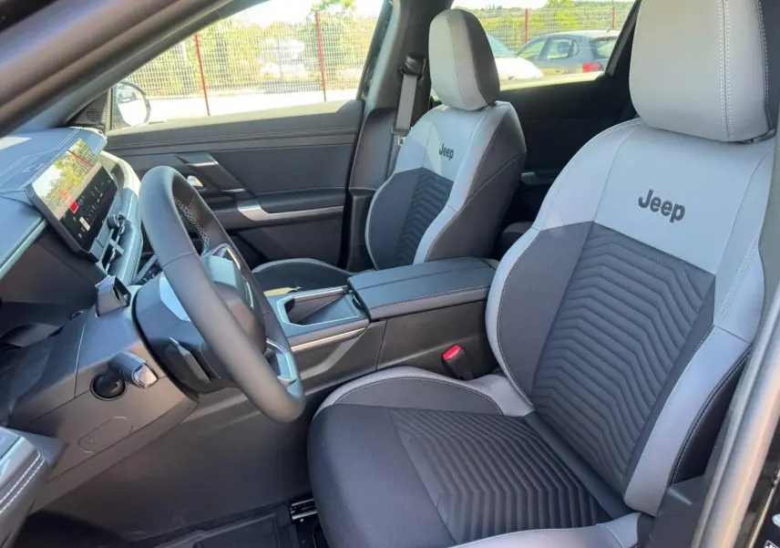 Vue intérieure avant droite du Jeep Compass 2026 avec sièges bi-ton gris et noir marqués Jeep, volant multifonction et console centrale.