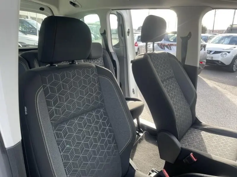 Vue intérieure des sièges avant en tissu gris à motifs géométriques du Peugeot Rifter blanc, porte latérale ouverte.