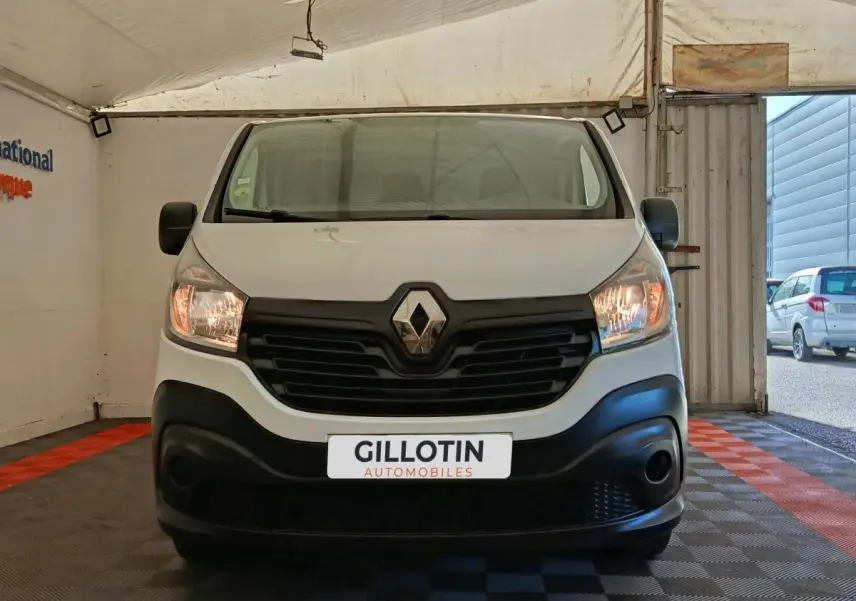 Vue frontale d'un Renault Trafic Fourgon blanc avec calandre noire et phares allumés dans un garage.