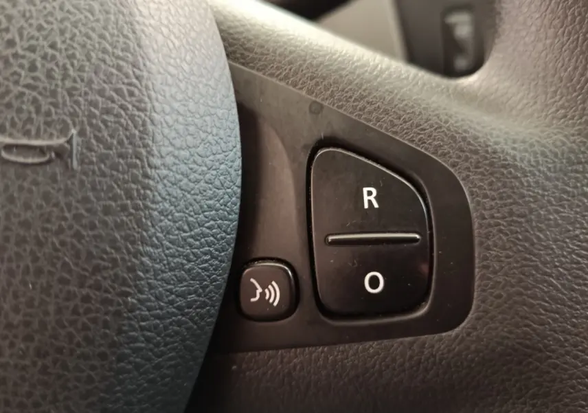 Gros plan sur les boutons de commande du volant noir du Renault Trafic Fourgon blanc, côté gauche.