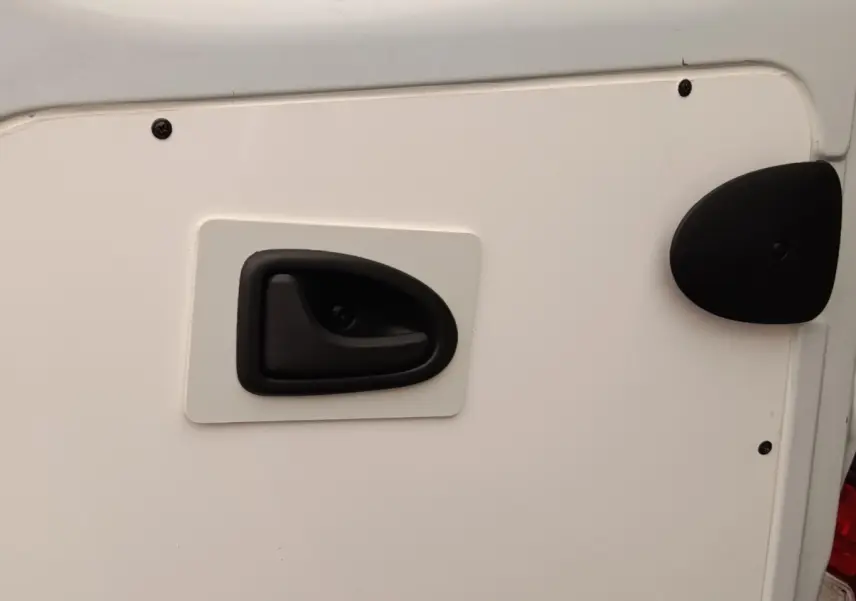 Gros plan sur la poignée de porte arrière noire d’un Renault Trafic Fourgon blanc, vue latérale droite.