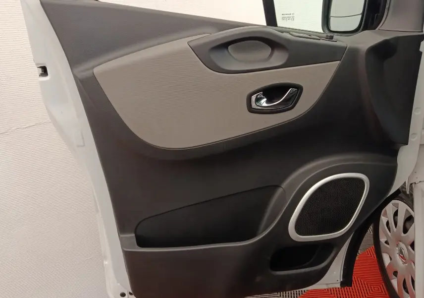 Vue rapprochée de la porte avant gauche blanche du Renault Trafic Fourgon avec poignée chromée et haut-parleur intégré.