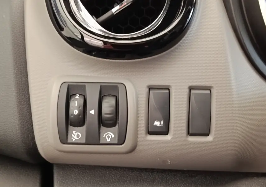 Gros plan sur les commandes de réglage des phares et de l'ESP sur le tableau de bord gris clair du Renault Trafic Fourgon blanc.