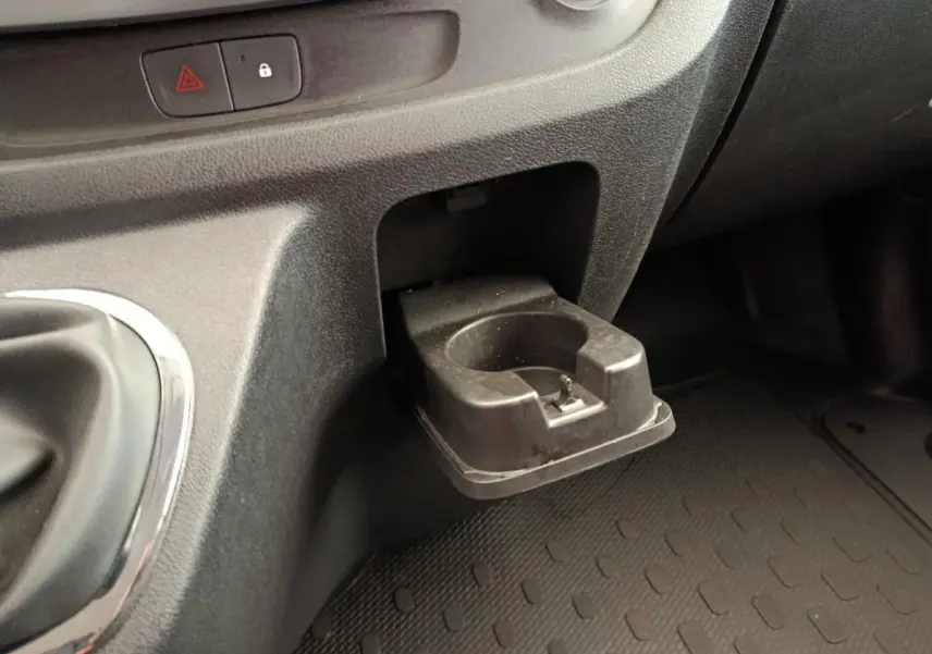 Gros plan sur le porte-gobelet noir escamotable côté passager du tableau de bord du Renault Trafic blanc.