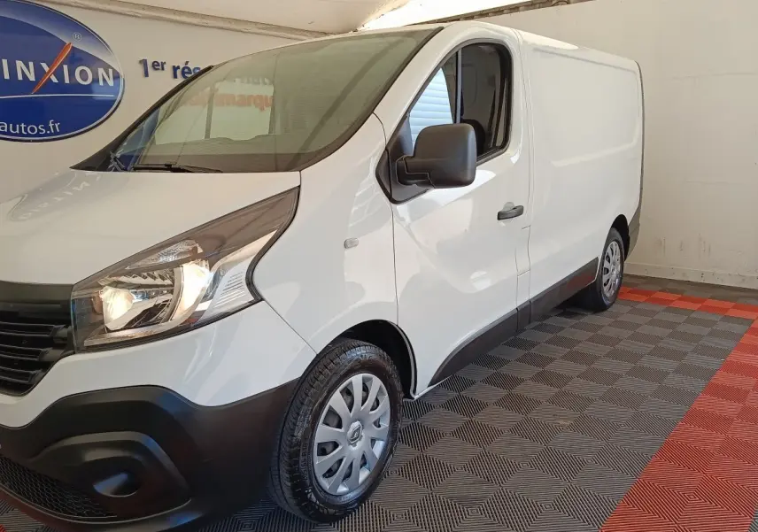 Renault Trafic Fourgon blanc vu en 3/4 avant droit, avec phares allumés et jantes acier grises.
