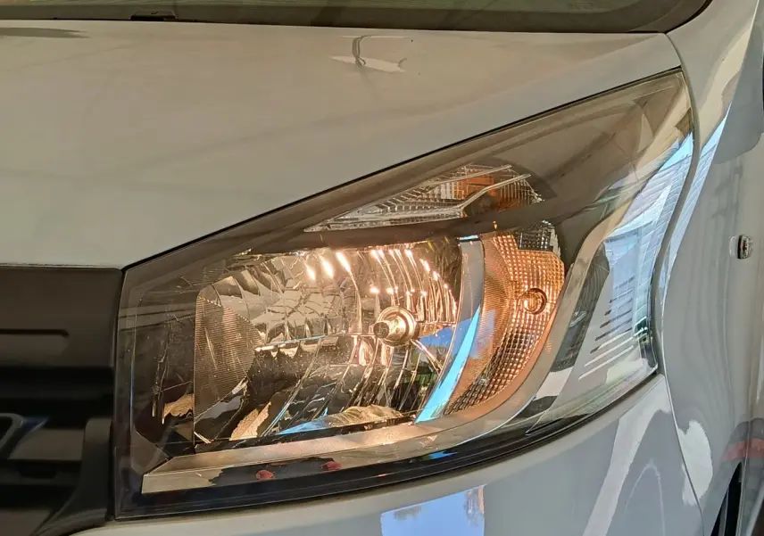 Gros plan sur le phare avant droit du Renault Trafic blanc, mettant en valeur le design halogène et la carrosserie brillante.