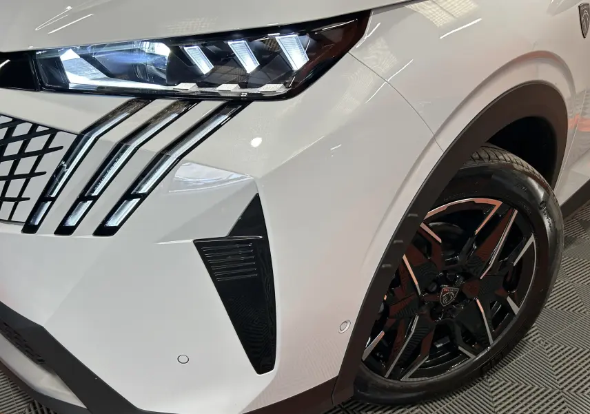 Gros plan sur l’avant droit blanc Okenite du Peugeot 3008 Hybrid 2026, avec phares LED et jante noire bi-ton.