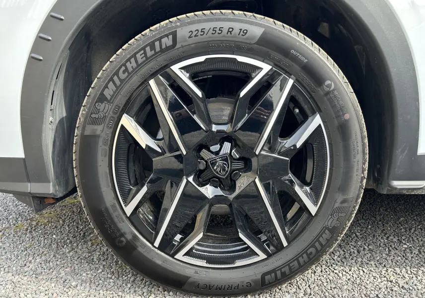 Gros plan sur la roue avant gauche d’un Peugeot 3008 blanc Okenite, jante alliage noire et argent avec pneu Michelin.