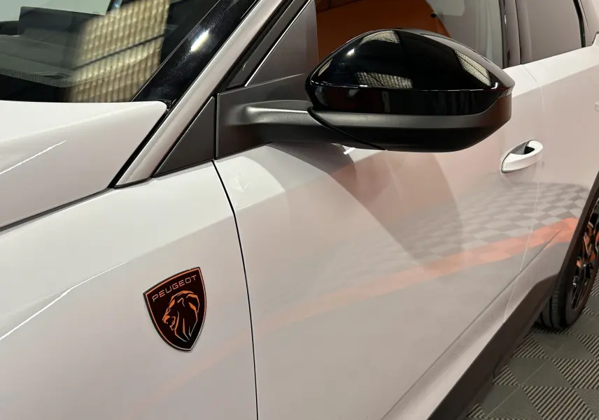 Détail du côté gauche blanc Okenite du Peugeot 3008 III Hybrid avec rétroviseur noir brillant et logo Peugeot bronze.