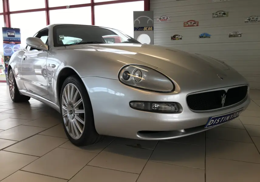Maserati Coupé gris clair vue 3/4 avant droit, mettant en valeur ses phares ovales et la calandre au trident distinctif.