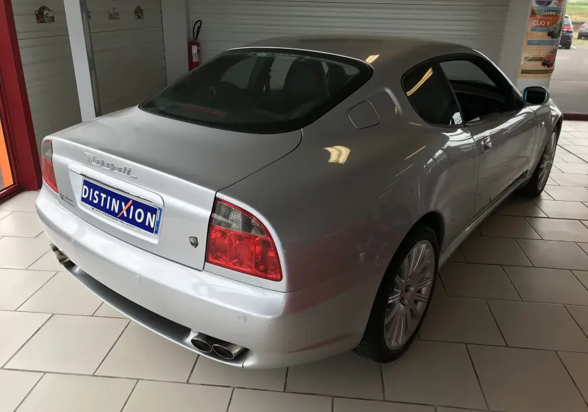 Vue 3/4 arrière droite d'une Maserati Coupé gris clair 2003 avec feux arrière rouges et double sortie d'échappement chromée.