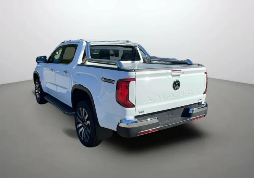 Volkswagen Amarok V6 blanc vu de l'arrière côté gauche, avec badge 4MOTION et benne équipée d'arceaux chromés.