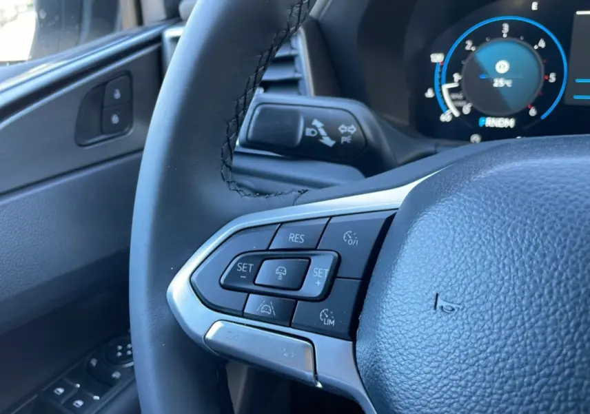 Gros plan sur le volant noir du Volkswagen Amarok 2025, montrant les commandes multifonctions côté gauche et le tableau de bord numérique.