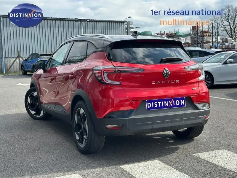 Vue 3/4 arrière d'un Renault Captur rouge flamme avec toit noir et jantes alu noires sur parking.