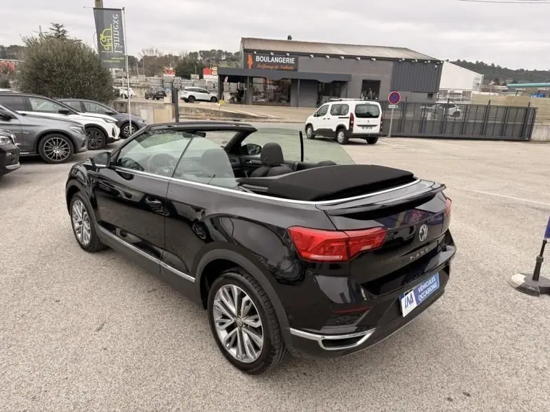 Volkswagen T-Roc Cabriolet noir métal vue 3/4 arrière côté gauche, capote ouverte, jantes alliage visibles.