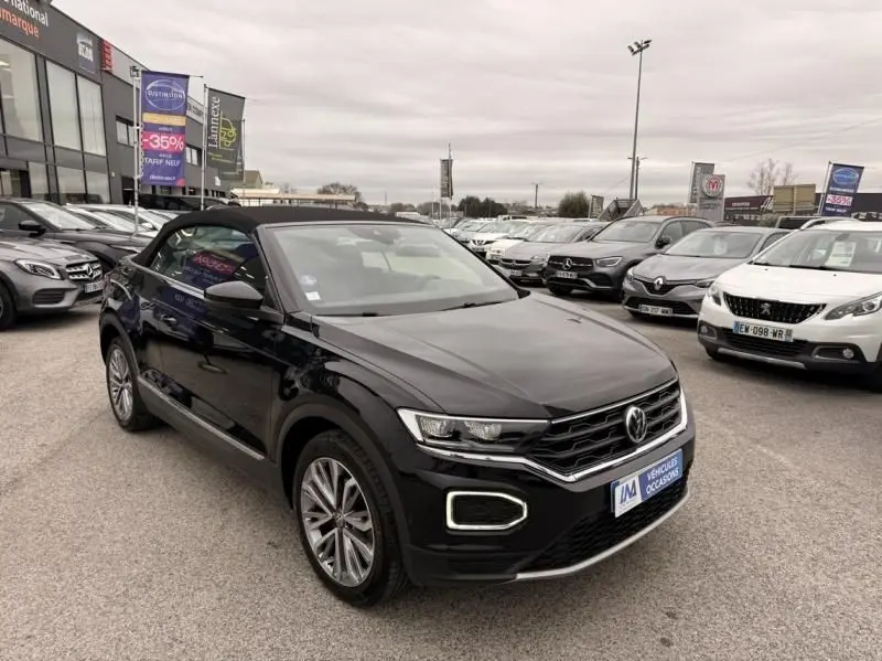 Volkswagen T-Roc Cabriolet noir métal vue 3/4 avant droit avec toit souple fermé sur parking extérieur.