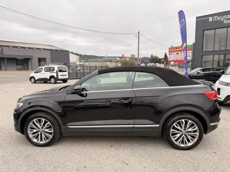 Vue de profil côté gauche d’un Volkswagen T-Roc Cabriolet noir métal avec capote noire, jantes alliage et lignes chromées.